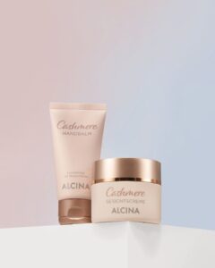 Tube 'Cashmere HANDBALM' und Tiegel 'Cashmere GESICHTSCREME' mit Markenname ALCINA vor pastellfarbenem Hintergrund.
