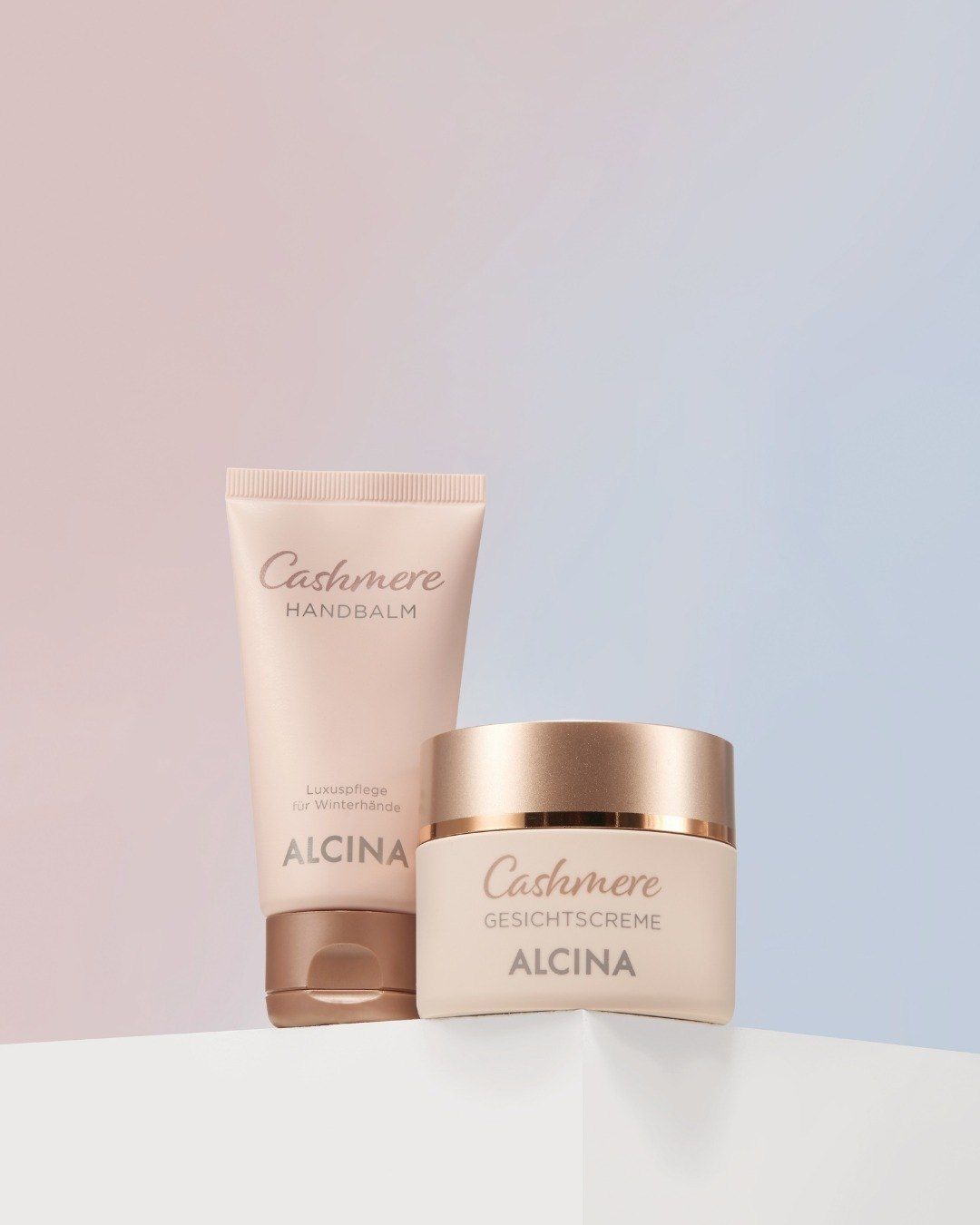 Tube 'Cashmere HANDBALM' und Tiegel 'Cashmere GESICHTSCREME' mit Markenname ALCINA vor pastellfarbenem Hintergrund.